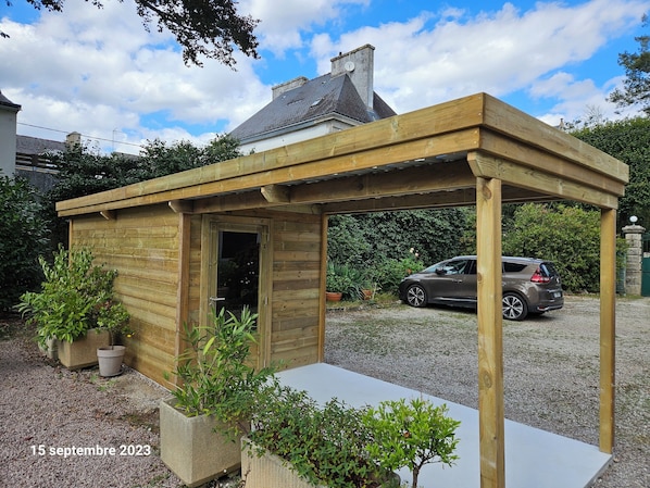 A wooden structure with a door, surrounded by potted plants and a gravel path. - L'Annexe (Pontivy)