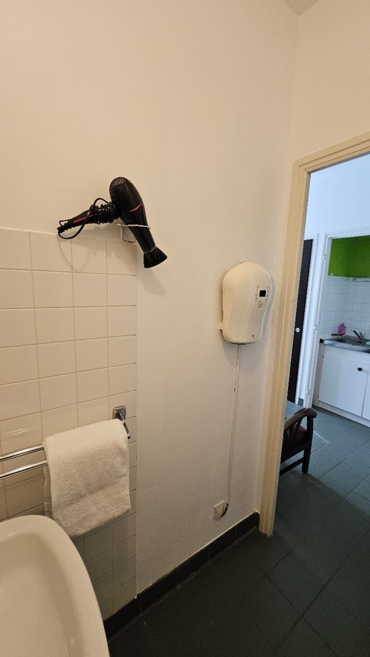 Une salle de bain équipée d’un porte-serviettes, d’un sèche-cheveux et d’un sèche-mains fixé au mur.