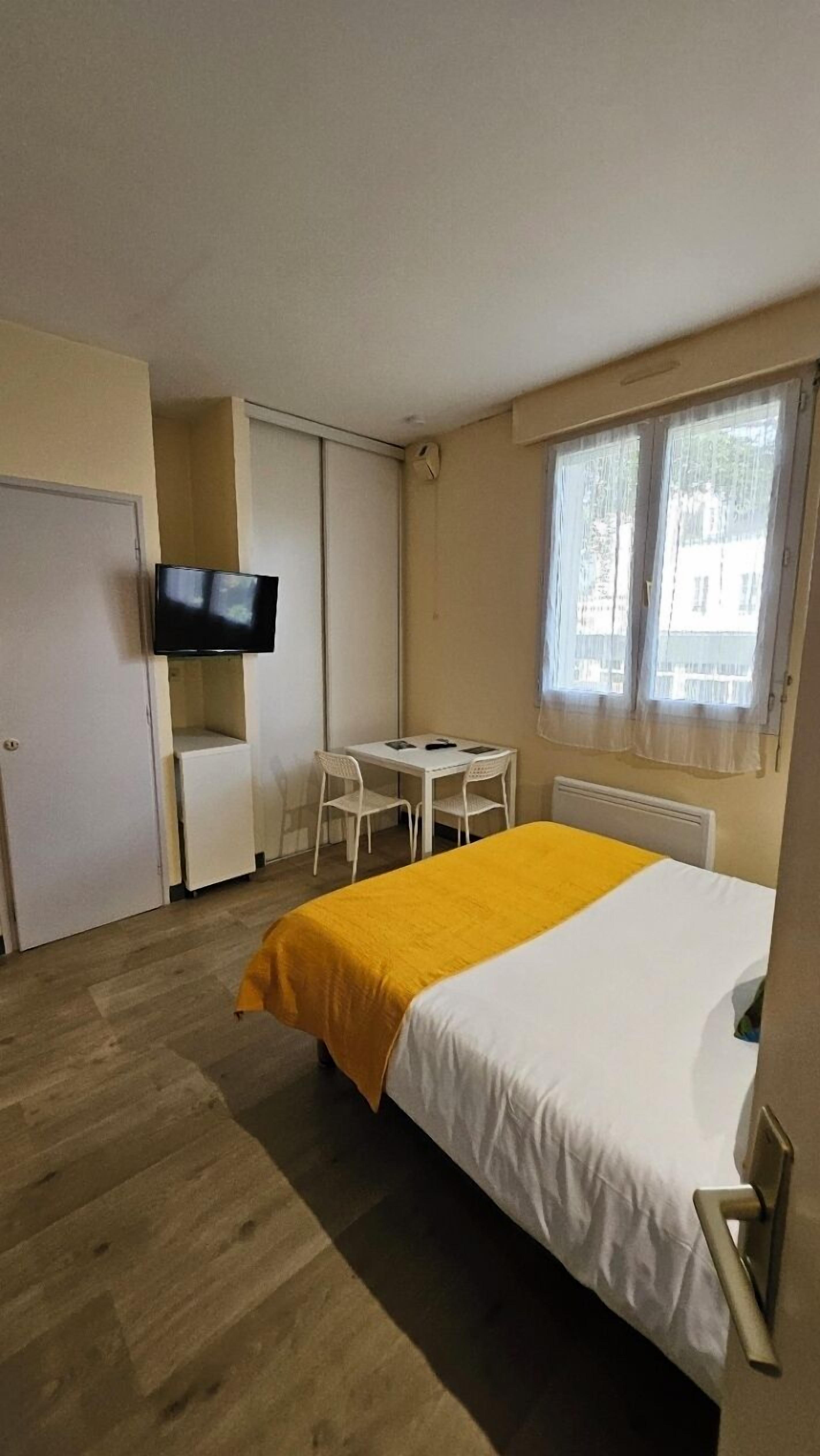 A hotel room with a bed, a desk, a chair, a television, and a window.