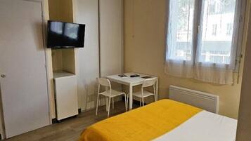 A hotel room with a bed, a desk, a chair, a television, and a window.