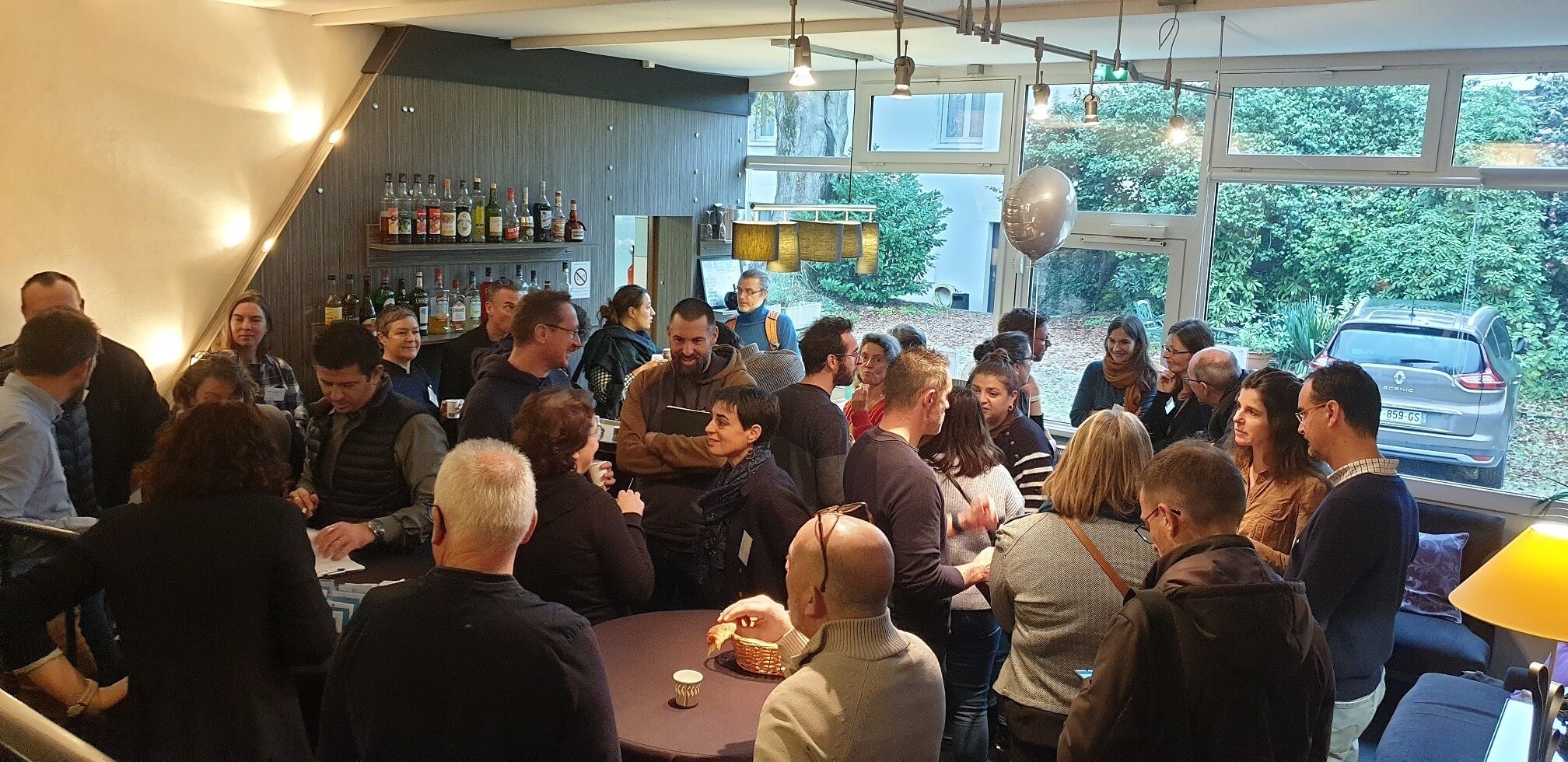 Un groupe de personnes s’est réuni dans un espace intérieur moderne, doté de grandes fenêtres et d’un bar.