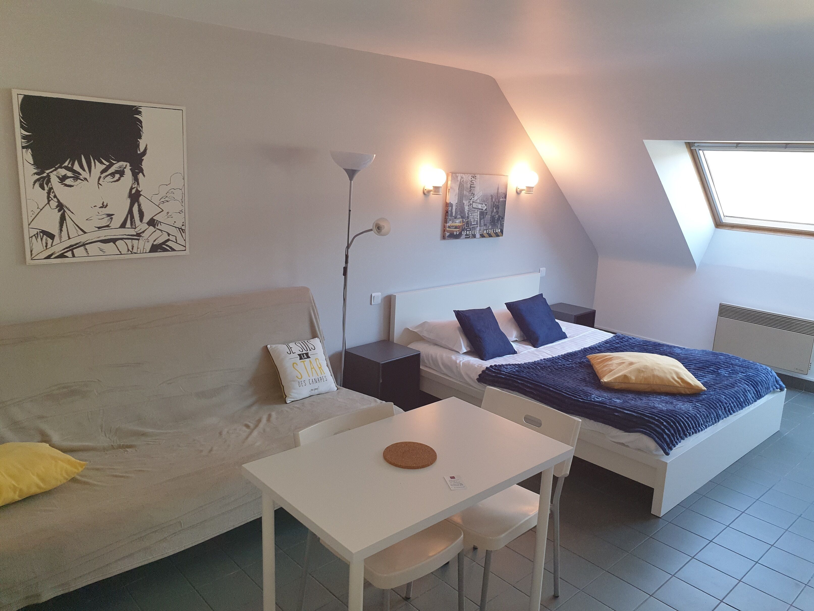 A bedroom with a bed, a white table, a couch, and a painting on the wall.