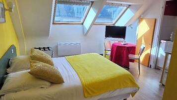 A bedroom with a bed, a desk, a chair, a TV, and two windows.