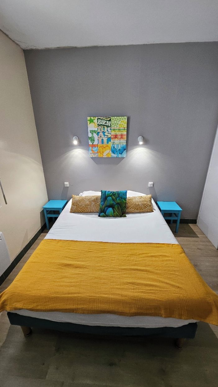 A bedroom with a bed, two nightstands, a wall art piece, and a yellow blanket.