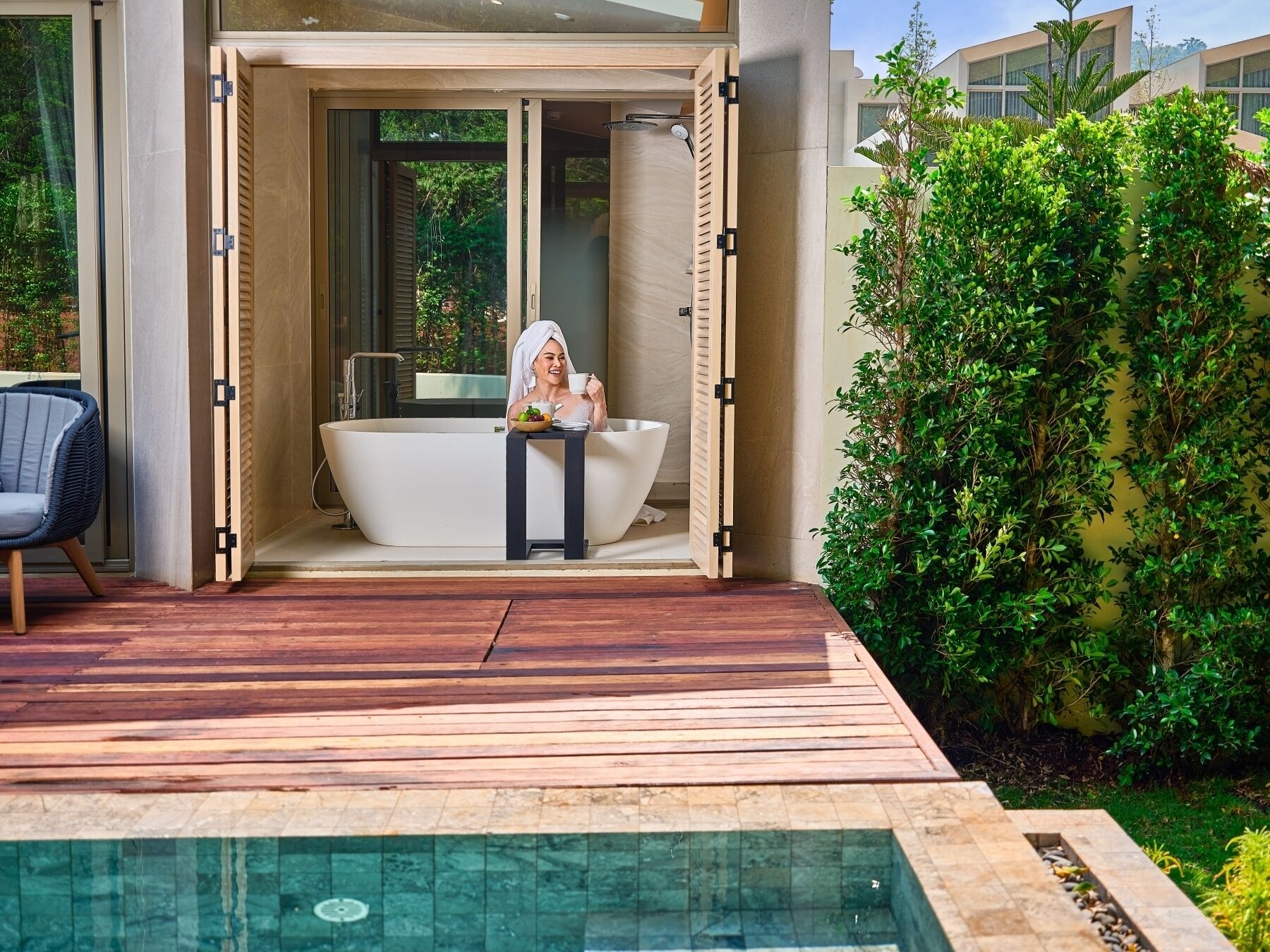Une salle de bain extérieure moderne avec une baignoire sur pieds, une petite table sur laquelle est posé un saladier rempli de fruits et une chaise.