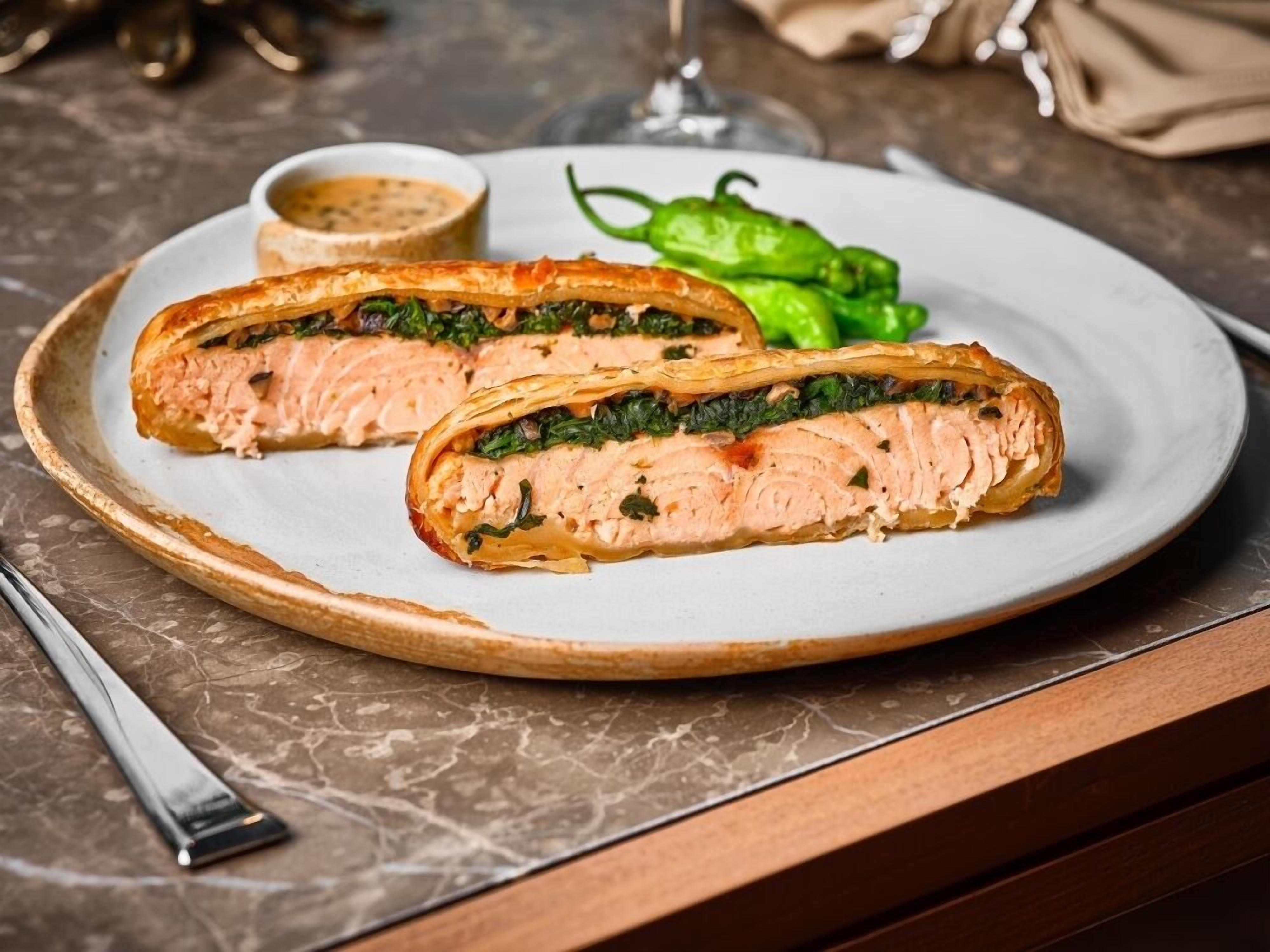 A plate with a salmon dish, a small bowl of sauce, and green peppers.