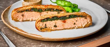 A plate with a salmon dish, a small bowl of sauce, and green peppers.