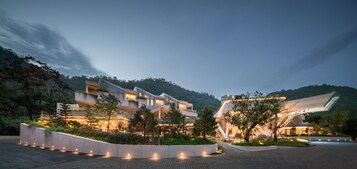 Un hotel moderno con varios pisos, iluminación exterior y un jardín ajardinado.