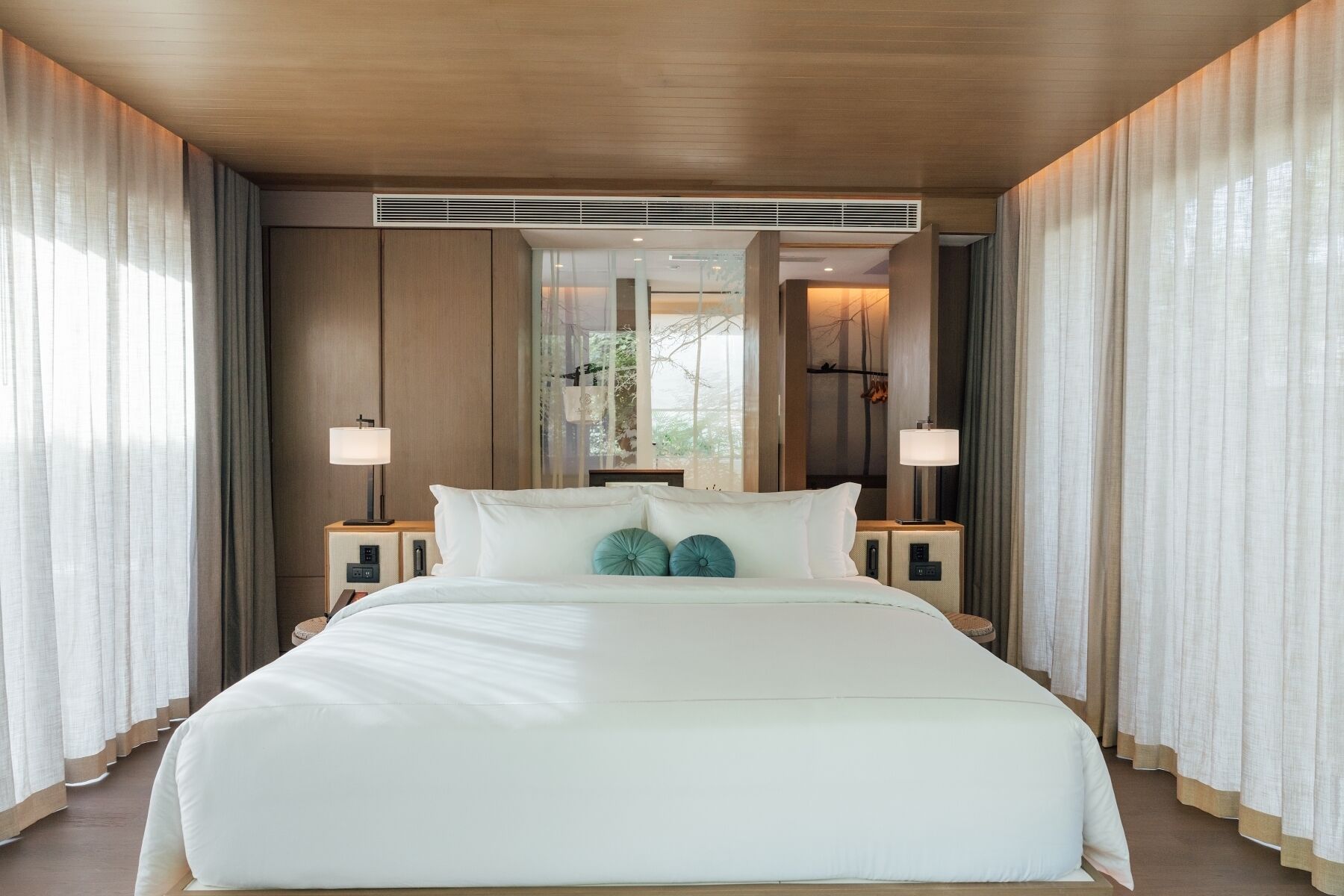 Una habitación de hotel moderna con una cama grande, dos mesitas de noche y un espejo grande sobre la cama.
