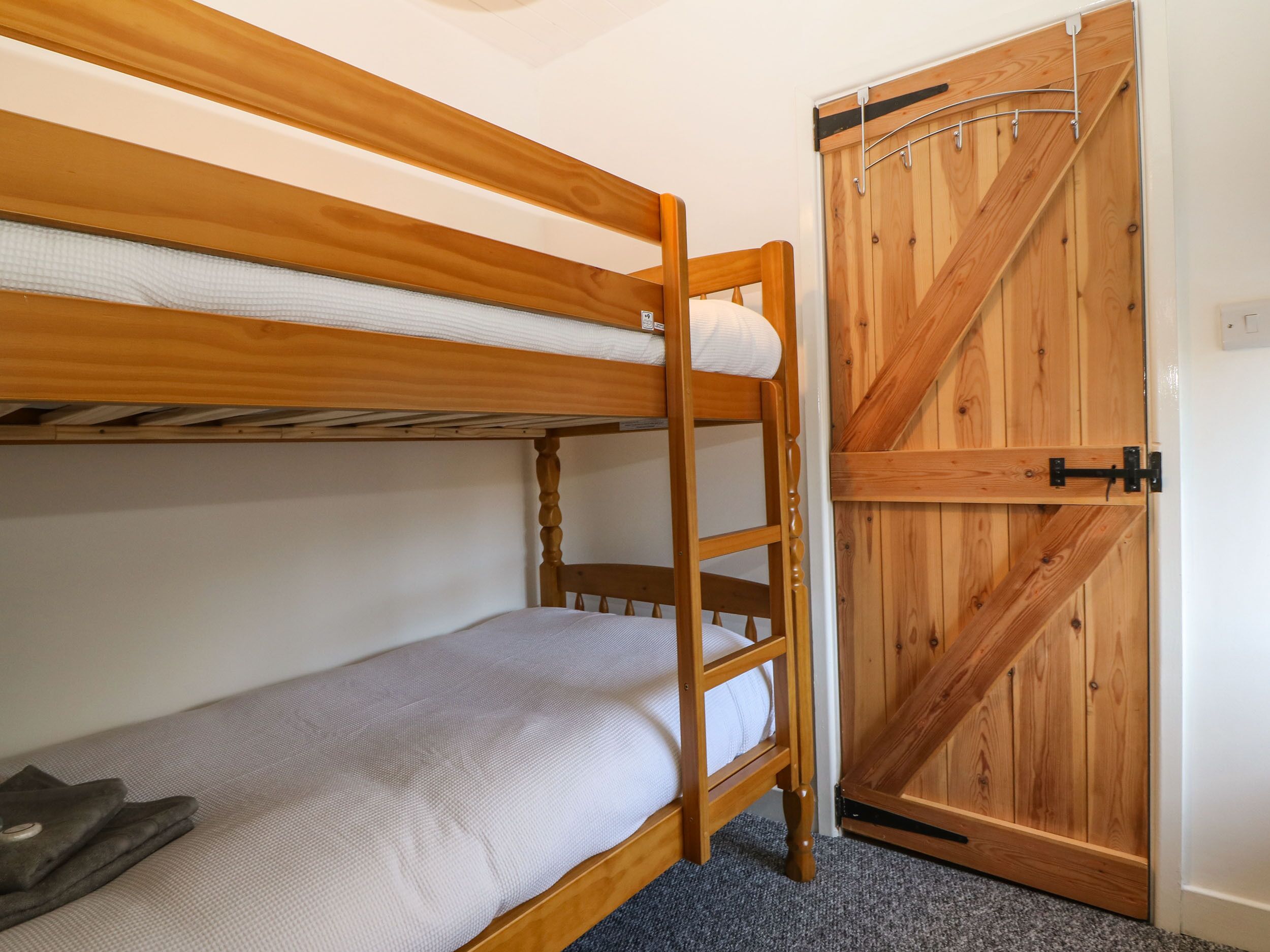 A bunk bed with a wooden ladder, a single bed below, and a wooden door with a metal handle.