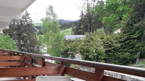 A balcony with a metal chair and wooden railing, overlooking a green landscape with trees and a distant building. - Courchevel 1550 Village 5-person apartment (Courchevel)