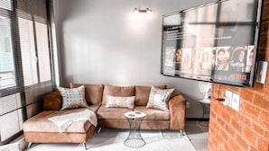 A living room with a sectional sofa, a small side table, and a flat-screen TV mounted on a brick wall.