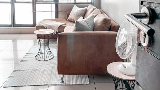 A modern living room with a sofa, two side tables, and a standing fan.