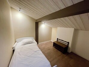 Een eenpersoonsbed met wit beddengoed in een kamer met houten vloer en een schuine balkenkap.