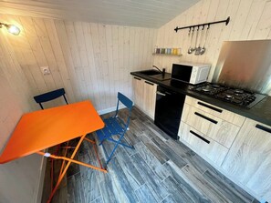 A compact kitchen with a gas stove, a microwave, and a sink. There is a small dining table with a chair.