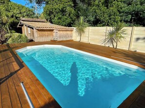 A rectangular swimming pool with clear blue water, surrounded by a wooden deck and a small wooden structure.