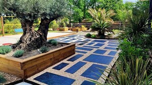 Un jardín con un árbol grande, un camino de piedra con diseño y diversas plantas.
