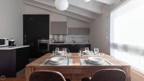 A modern kitchen with dark cabinets, a central island, and a dining area set for four with a wooden table and chairs. - Italianway Comfort - Rubens 19 B (Milan)
