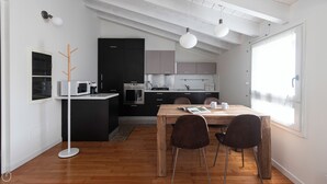 A modern kitchen with a dining area, featuring a wooden table, two chairs, and a view of the city through large windows. - Italianway Comfort - Rubens 19 B (Milan)