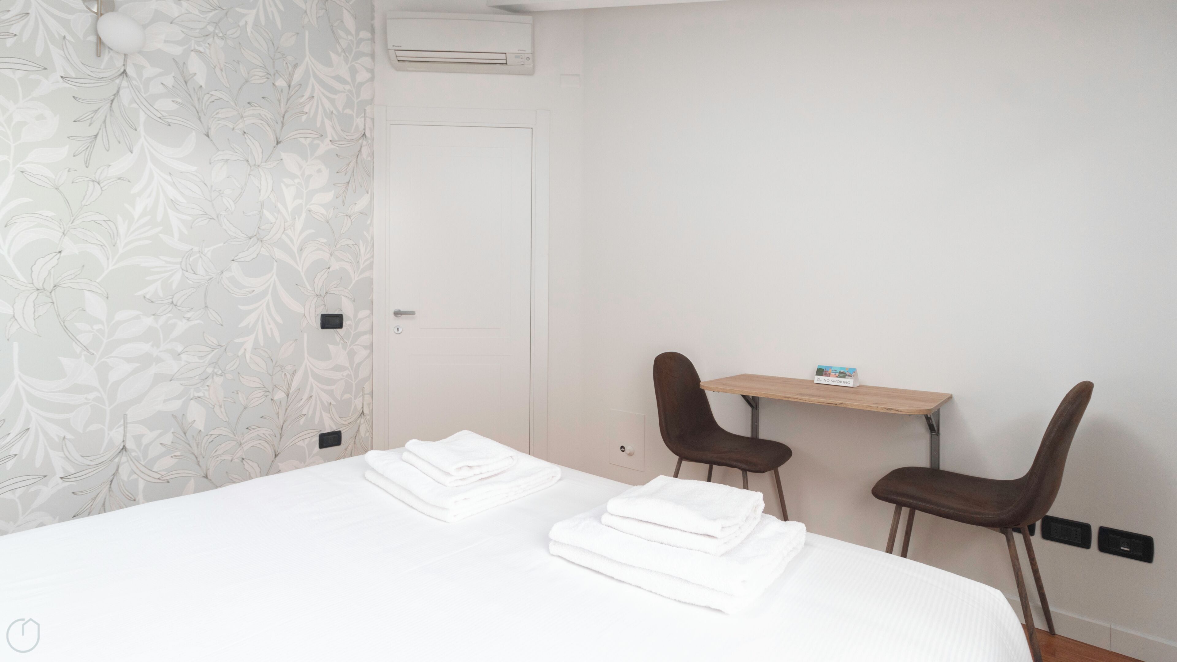A hotel room with a bed, two chairs, a small table, and a door.