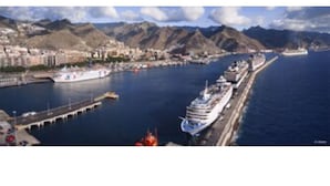 Une ville côtière où un grand navire de croisière est amarré à un quai, entourée de montagnes et surplombée d’un ciel dégagé.