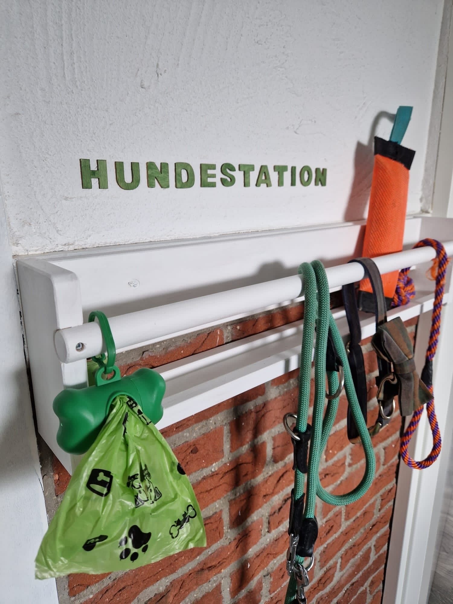 Un muro con la scritta "HUNDESTATION" e un portachiavi per guinzagli da cane con diversi oggetti.