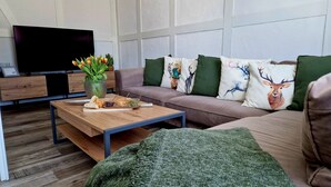 A modern living room with a sofa, decorative pillows, a coffee table with snacks, a TV, and a potted plant.