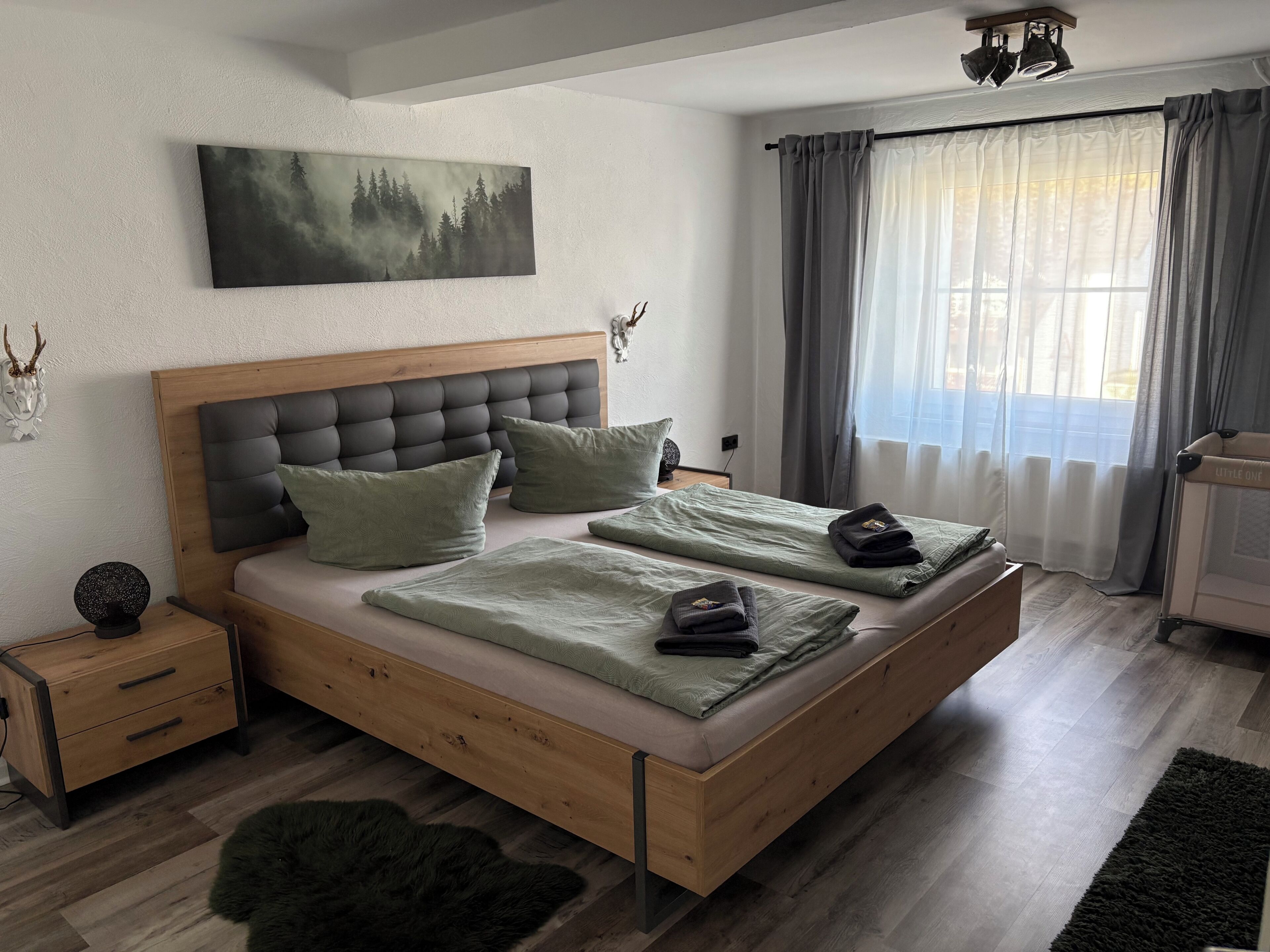 Una camera da letto con un letto, un comodino, un quadro appeso al muro, una finestra con tende e una testiera.