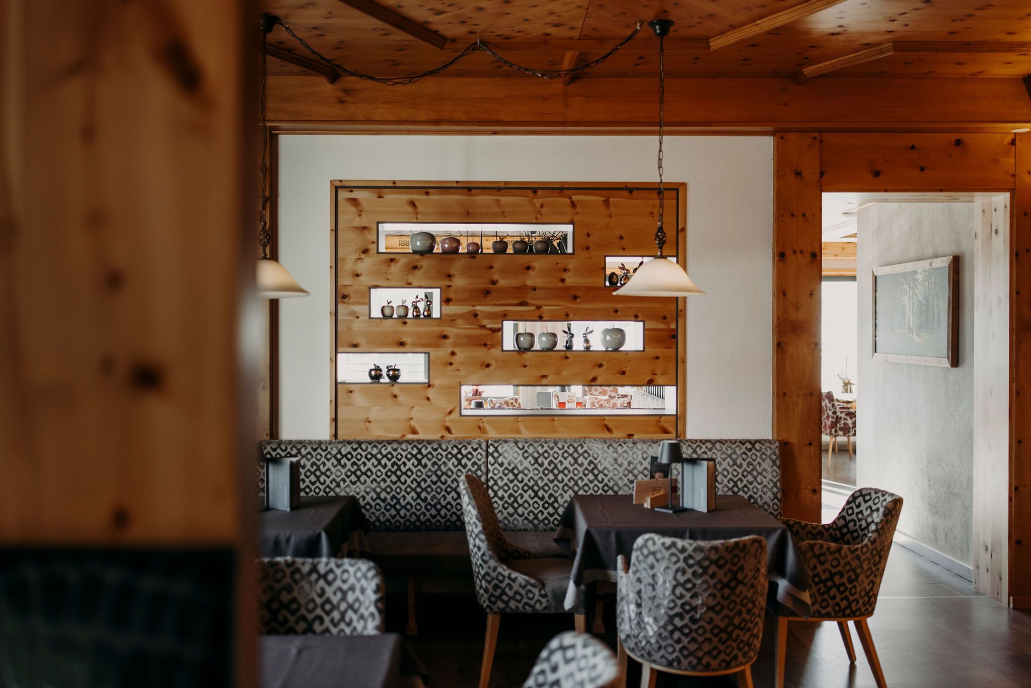 A cozy restaurant with wooden walls, patterned seating, and a central table with chairs.