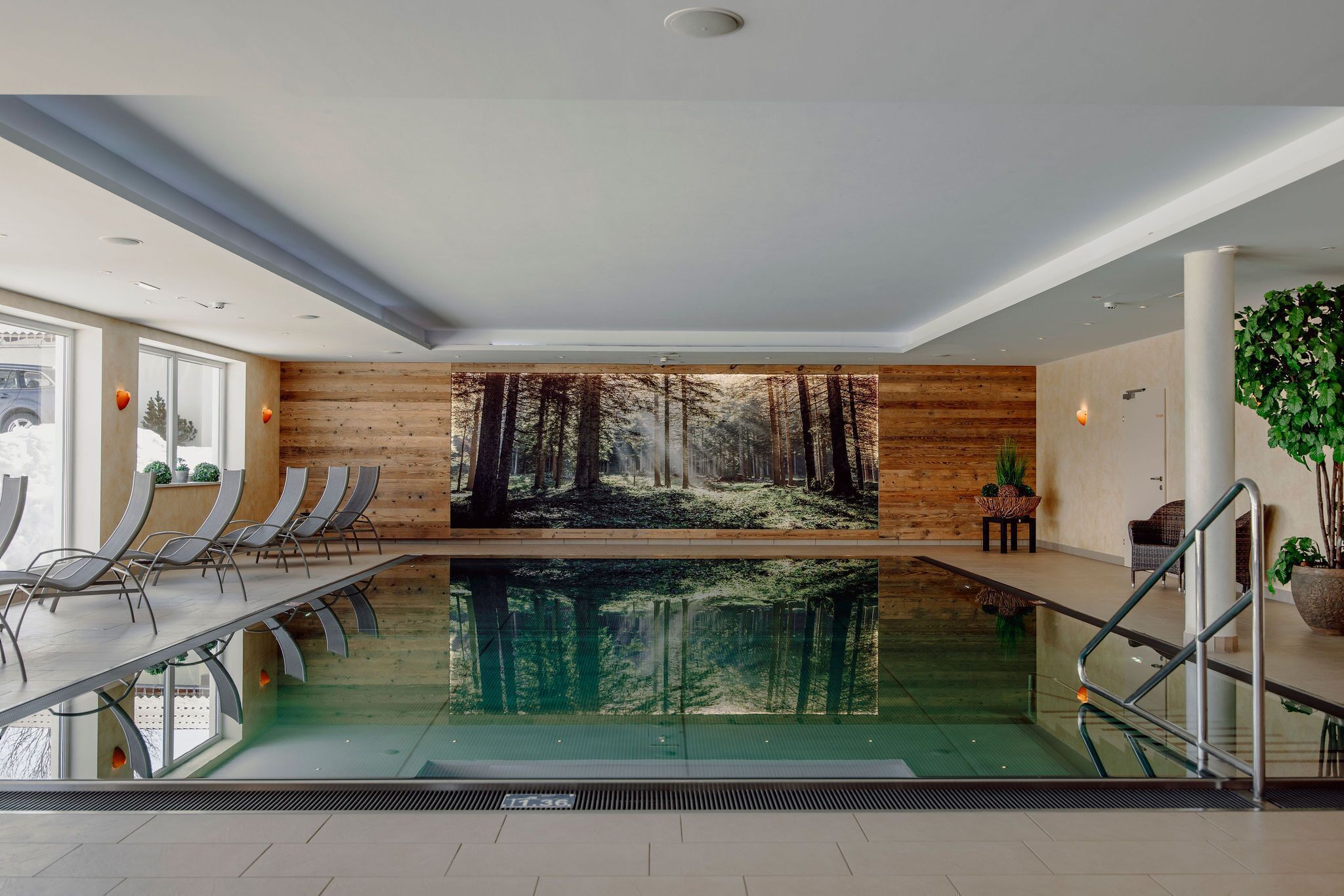 Piscina interior moderna com painel de parede de madeira, área de estar e plantas em vasos.