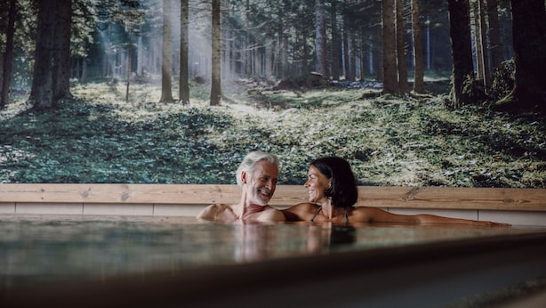 Un couple se détend dans une piscine à débordement en bois, avec vue sur la forêt.