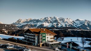 Un hôtel à la façade verte et blanche, doté de nombreux balcons et offrant une vue sur des montagnes enneigées.