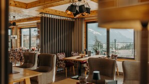 Un espace repas avec une table et des chaises en bois, de grandes fenêtres offrant une vue sur les montagnes et un lustre moderne.