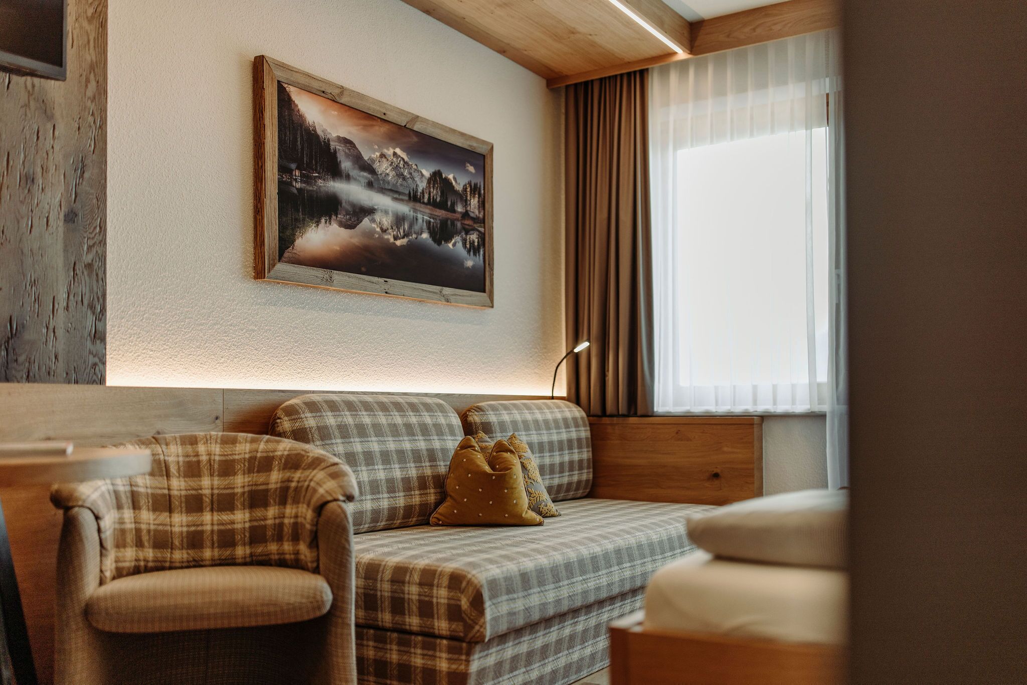 Una sala de estar acogedora con un sofá, un sillón y un cuadro de un paisaje montañoso.