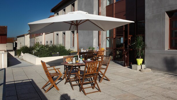 An outdoor patio with a table set for dining, surrounded by wooden chairs and a large white umbrella. - Romantic Getaway in Carcassonne (Carcassonne)