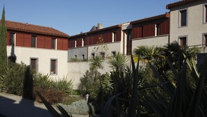 A courtyard with buildings, a pathway, and various plants. - Romantic Getaway in Carcassonne (Carcassonne)