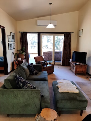 Ein Wohnzimmer mit einem grünen Sofa, einem Holztisch, einem Fernseher und einer Gitarre.