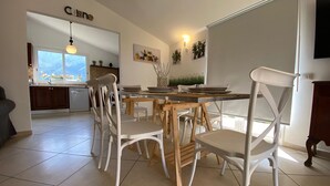 Un'area pranzo con sedie bianche e un tavolo in legno, una cucina con lavastoviglie e un cartello che riporta la scritta "Cuisine".