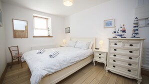 Un dormitorio con cama, cómoda, silla, ventana y lámpara.