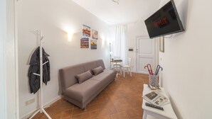 Un salon comprenant un canapé, un porte-manteau, une table avec une télécommande et un téléviseur fixé au mur qui affiche le logo « NETFLIX ».