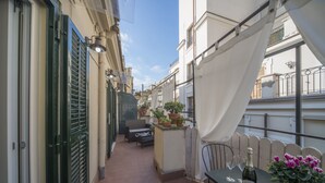 Un étroit couloir extérieur avec un canapé, une table sur laquelle se trouvent une bouteille et des verres, et des plantes en pot.
