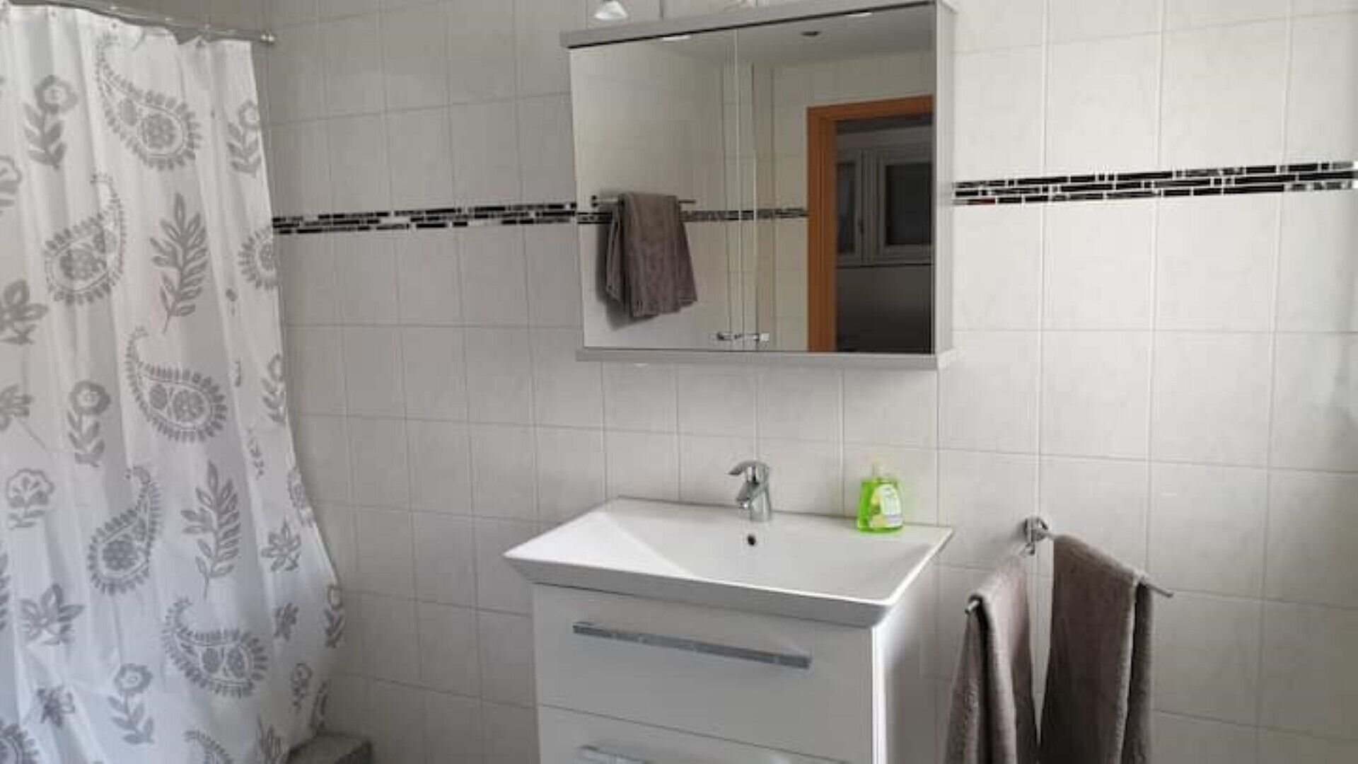 Un baño con un lavabo blanco, un espejo encima y una cortina de ducha con estampado floral.