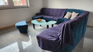 A living room with a blue sofa, a matching ottoman, and a glass coffee table. - Großzügige Ferienwohnung in Heßheim (Heßheim)