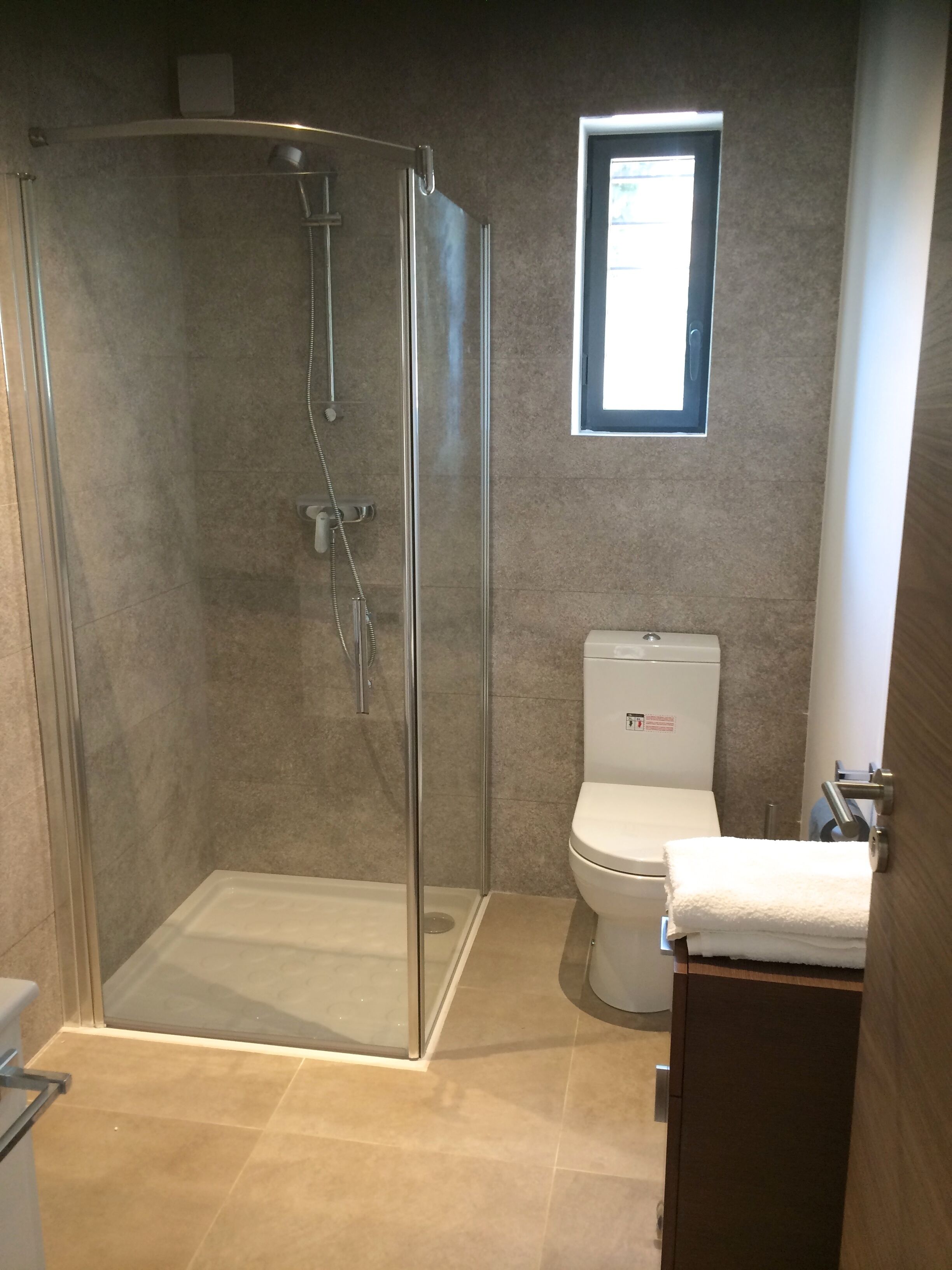A bathroom with a glass-enclosed shower, a toilet, and a small window.