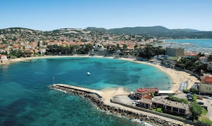 An aerial view of a coastal town with a sandy beach, clear blue waters, and a mix of residential and commercial buildings.