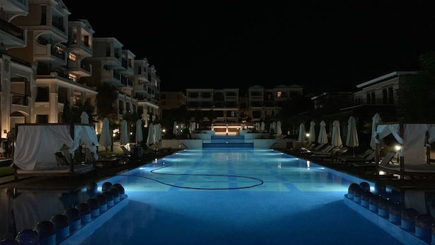 A swimming pool at night with lounge chairs and umbrellas on either side. - Sozopol Green life Apartment (Созопол)