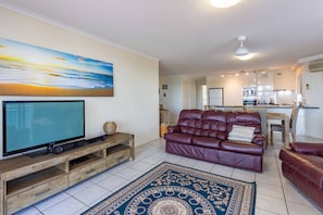 A modern living room with a flat-screen TV, leather sofa, and a patterned rug.