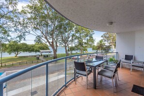 A balcony with a table and chairs, overlooking a body of water and trees.