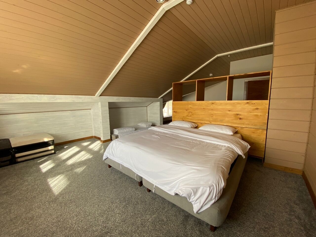 Ein Schlafzimmer mit schrägem Dach, einem Bett mit weißer Bettwäsche, einem Holzkopfende und einer eingebauten Sitzbank.