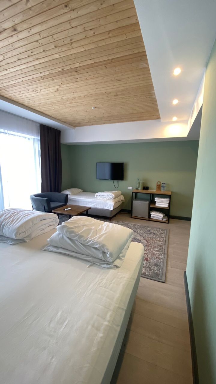 Hotellihuone, jossa on puinen katto, sänky, työpöytä, tuoli, televisio ja pieni kaappi, jossa on pyyhkeitä.